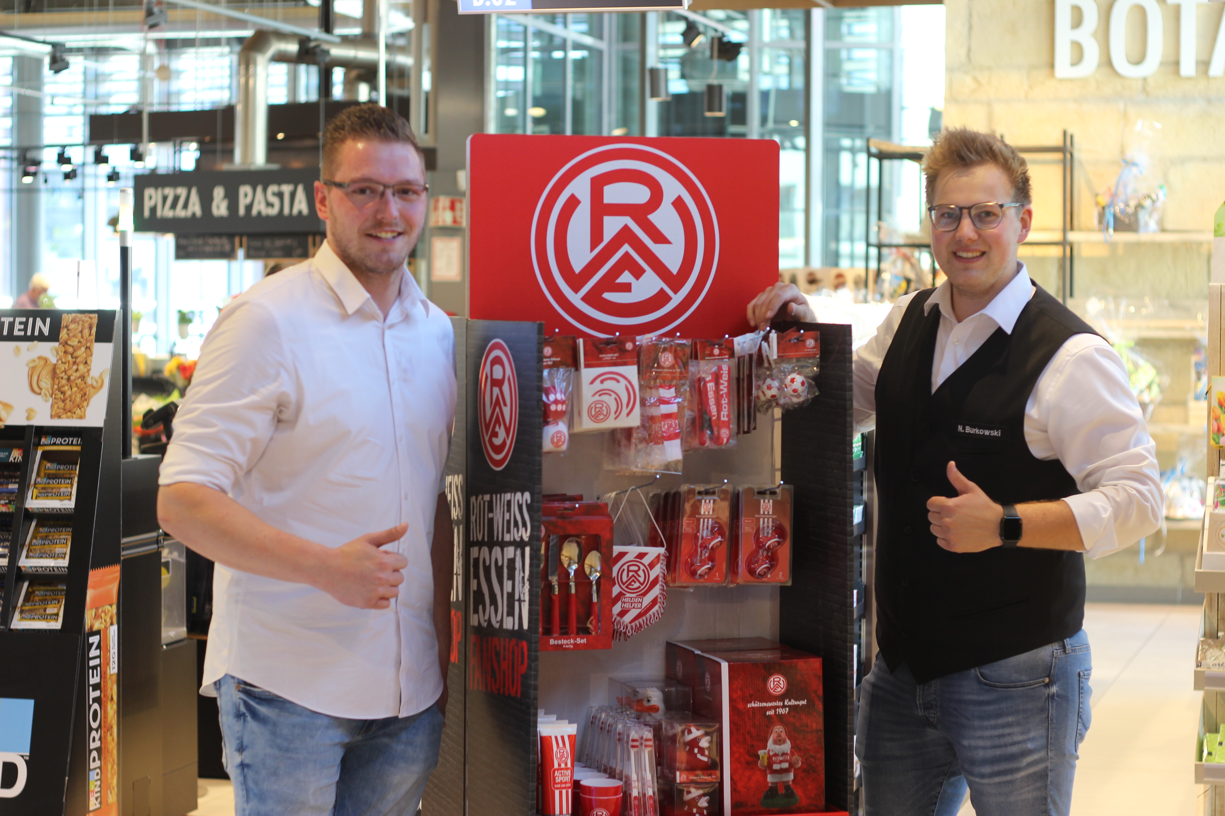 Patrick Metz (l., Merchandising RWE) und Nico Burkowski (r., Filialleiter Altendorfer Straße) präsentieren den mobilen Fanshop.